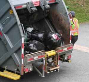 Back of garbage truck filled with black trash bags.
