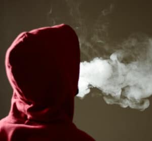 Person in red hoodie blowing smoke from e-cigarette.